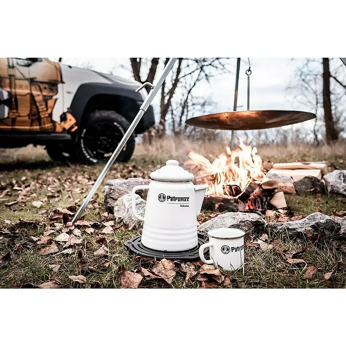 Petromax Tasse - 370 ml, Weiß - Ein Petromax Perkolator und eine Tasse stehen neben einem Lagerfeuer, mit einem Auto im Hintergrund. Ideal für Outdoor-Abenteuer.