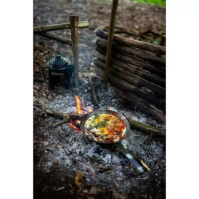 Petromax Grillpfanne - Durchmesser: 20,5 cm - 28 cm, Höhe: 15 cm, Eisen - Eine brutzelnde Pfanne mit Eiern und Gemüse über einem Lagerfeuer, daneben ein dunkler Kessel.