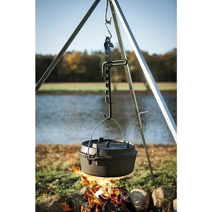 Petromax Dutch Oven - Ø x H: 36,4 x 16 cm, Gusseisen, 5,5 l, Planer Boden - Ein Dutch Oven hängt an einem Dreibein über einem Lagerfeuer, ideal zum Kochen im Freien. Die robuste Konstruktion verspricht Langlebigkeit.