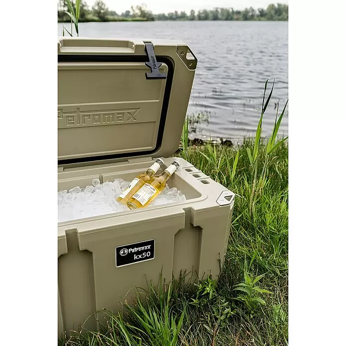 Petromax Kühlbox - Sand, 50 l, L x B x H: 68,5 x 48,5 x 50 cm - Beigefarbene Petromax kx50 Kühlbox, offen mit Eis und zwei Flaschen, steht im Gras an einem See.