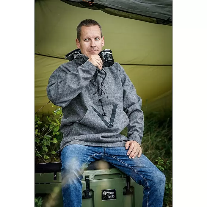 Petromax Sitzkissen - Passend für: Petromax Kühlbox 50 l, L x B x H: 46,5 x 66 x 5,5 cm, Schwarz - Mann in grauem Anorak trinkt aus schwarzem Becher, sitzt auf grüner Petromax kx50 Kühlbox.
