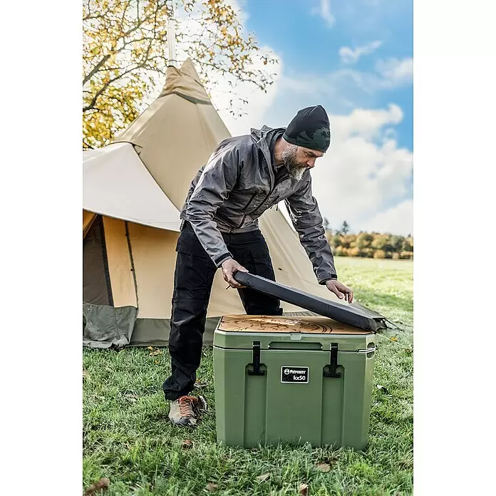 Petromax Sitzkissen - Passend für: Petromax Kühlbox 50 l, L x B x H: 46,5 x 66 x 5,5 cm, Schwarz - Grüner Petromax kx50 Kühler wird von einem Mann im Freien neben einem Zelt geöffnet.