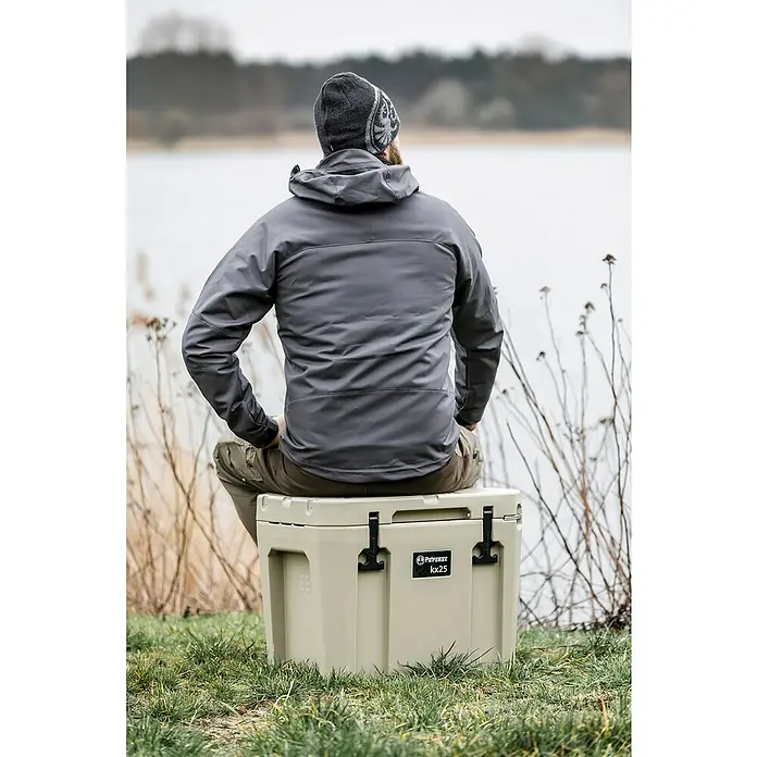 Petromax Kühlbox - Sand, 25 l, L x B x H: 58 x 40,5 x 45 cm - Ein Mann sitzt auf einer Petromax Kühlbox KX25 in der Natur, genießt die Aussicht und die Ruhe. Die robuste Kühlbox ist ideal für Outdoor-Abenteuer.