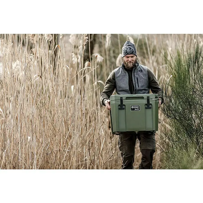 Petromax Kühlbox - Oliv, 25 l, L x B x H: 58 x 40,5 x 45 cm - Mann trägt eine grüne Protexx Kühlbox Loc25 durch hohes Gras. Ideal für Outdoor-Aktivitäten, um Lebensmittel und Getränke kühl zu halten.