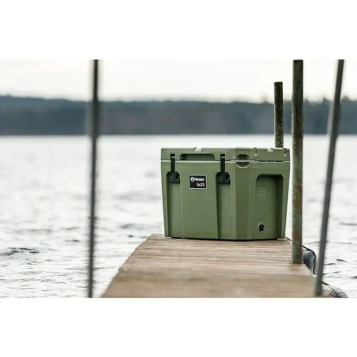 Petromax Kühlbox - Oliv, 25 l, L x B x H: 58 x 40,5 x 45 cm - Olivegrüne Petromax Kühlbox kx25 auf einem hölzernen Steg am See. Robuste Konstruktion für Outdoor-Abenteuer und zuverlässige Kühlung.
