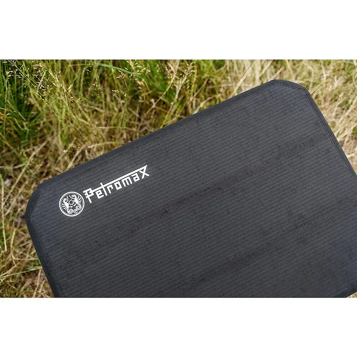 Petromax Sitzkissen - Passend für: Petromax Kühlbox 25 l, L x B x H: 38,5 x 56 x 5,5 cm, Schwarz - Nahaufnahme eines schwarzen Petromax Sitzkissens mit Logo auf einer Wiese.