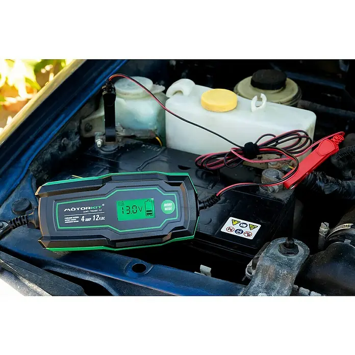 Arrancador de baterías - Capacidad: 120 Ah, 12 V - Un cargador de batería MotorKit de 4 Amp 12V está cargando la batería de un coche. El cargador es verde y negro, con pantalla digital.