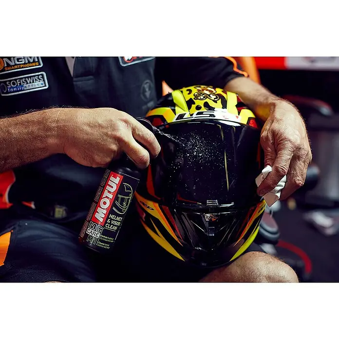 Limpiador específico para casco M1 y M2 - 500 ml, Apto para: Cascos de motocicleta - Un hombre limpia la visera de un casco de moto con el limpiador de cascos y viseras Motul para una visión clara y cuidado.