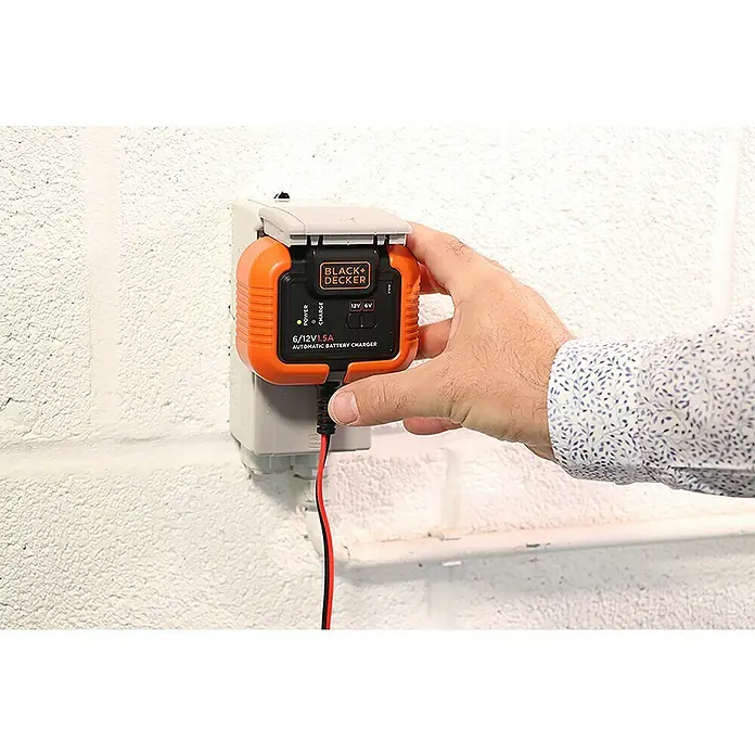 Black+Decker Arrancador de baterías - Capacidad: 70 Ah, 12 V - Un cargador de batería automático Black+Decker 6/12V 1.5A está siendo operado por una mano en un enchufe de pared.