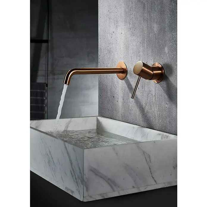 Camargue Natur Grifo de lavabo empotrado - Oro rosa - Primer plano de un lavabo moderno con un elegante grifo de cobre montado en la pared vertiendo agua. El lavabo es de mármol.