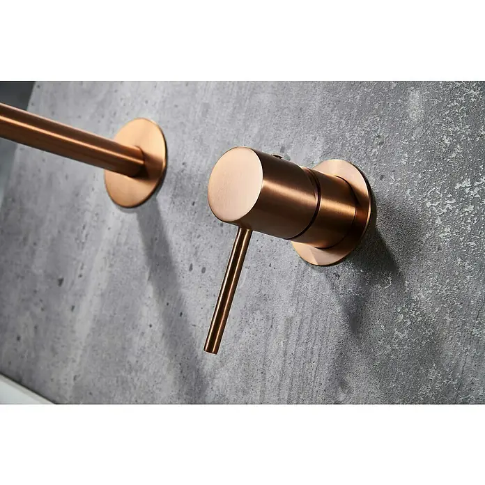 Camargue Natur Grifo de lavabo empotrado - Oro rosa - Primer plano de un elegante grifo de pared con acabado en cobre sobre una pared de hormigón gris. Diseño elegante para baños modernos.