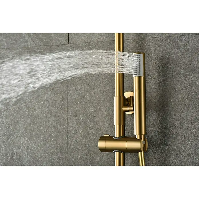 Camargue Natur Sistema de ducha - Con grifo termostático, Oro - Sistema de ducha de acero inoxidable dorado con chorro de agua frente a una pared gris. Diseño elegante para baños modernos.