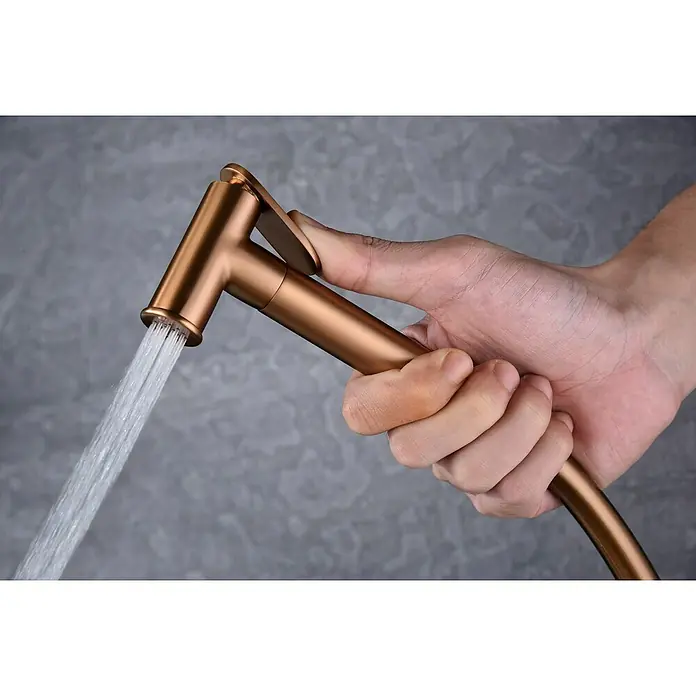 Camargue Natur Ducha higiénica inodoro - Oro rosa - Mano sujetando un rociador de bidé de bronce con agua saliendo. El producto es ideal para la higiene personal y ofrece un fácil manejo.