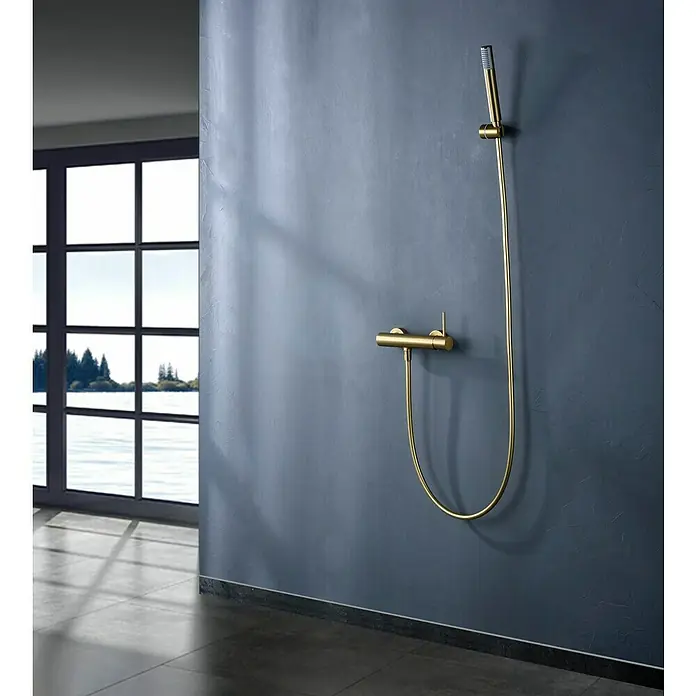 Camargue Natur Grifo monomando de ducha - Oro - Elegante conjunto de ducha dorado montado en una pared azul oscuro texturizada, con una gran ventana al fondo.