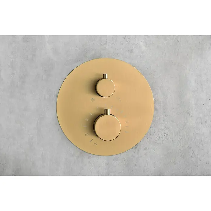 Camargue Natur Sistema de ducha empotrado - Con grifo termostático, Oro cepillado - Primer plano de un termostato de ducha redondo dorado con dos mandos de control montado en una pared gris.