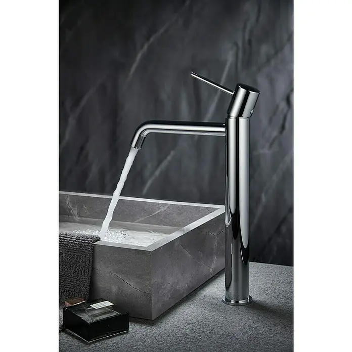 Camargue Natur Grifo de lavabo alto - Cromo - Elegante grifo de baño cromado vertiendo agua en un baño moderno con superficie de mármol gris.