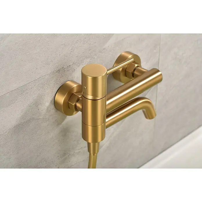 Camargue Natur Grifo monomando de bañera / ducha - Oro - Primer plano de un moderno grifo de baño dorado montado en una pared de azulejos grises. El diseño es minimalista y elegante.