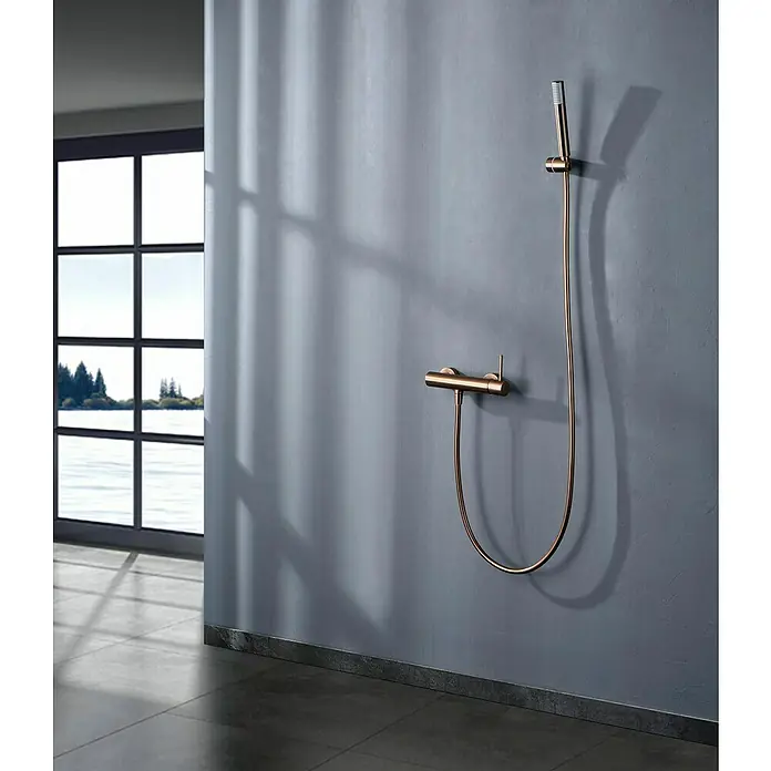 Camargue Natur Grifo monomando de ducha - Oro rosa - Elegante grifo de ducha dorado sobre una pared gris. El diseño es minimalista y moderno, perfecto para un baño elegante.
