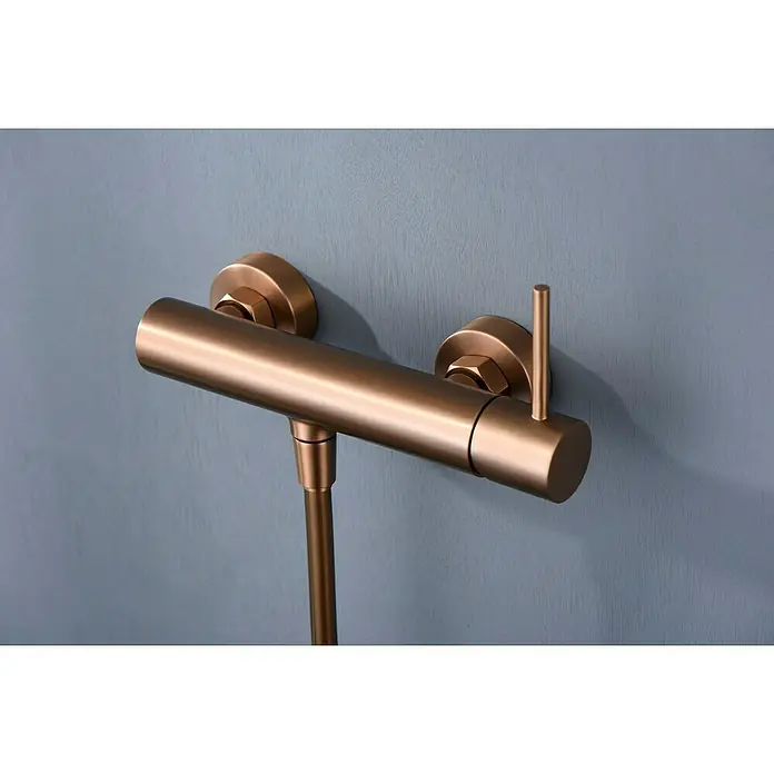 Camargue Natur Grifo monomando de ducha - Oro rosa - Primer plano de un moderno grifo de ducha de bronce sobre una pared azul grisáceo, que muestra un diseño de baño elegante y una alta calidad artesanal.