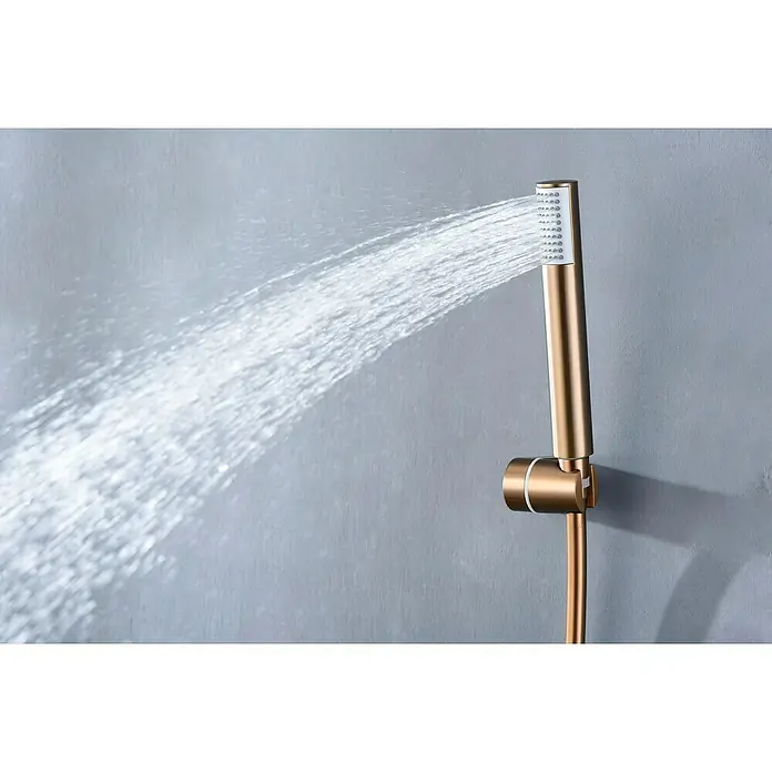 Camargue Natur Grifo monomando de ducha - Oro rosa - Primer plano de un cabezal de ducha de mano dorado rociando agua sobre un fondo gris. Diseño elegante para baños modernos.