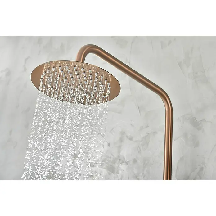 Camargue Natur Sistema de ducha - Con grifo monomando, Oro rosa - Primer plano de un moderno cabezal de ducha redondo de cobre que libera chorros de agua sobre un fondo claro y texturizado.
