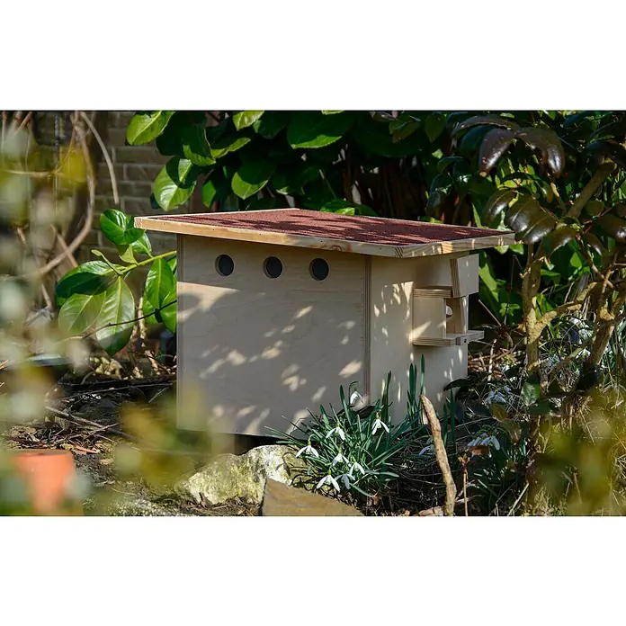 Dobar Nistkasten für Hummeln - L x B x H: 51 x 43 x 36 cm, Braun/Rot, Holz - Hölzernes Insektenhotel mit rotem Dach, umgeben von Grünpflanzen im Garten, bietet einen sicheren Unterschlupf für nützliche Insekten.