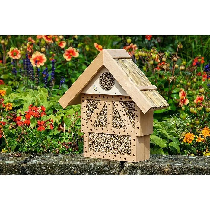 Dobar Insektenhotel Monschau - L x B x H: 37,5 x 15 x 38,5 cm, Natur - Nahaufnahme eines hölzernen Insektenhotels mit Röhrenfüllung vor einem Hintergrund aus bunten Blumen.