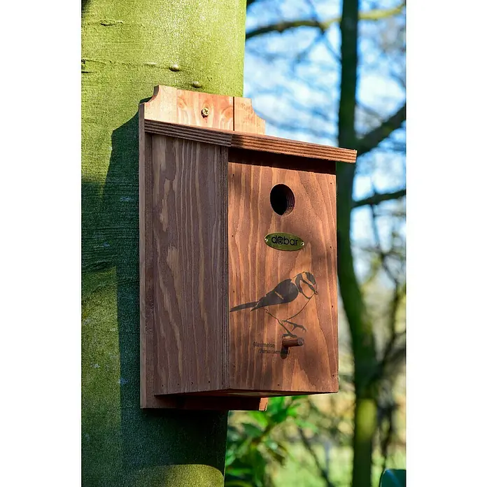Dobar Nistkasten - L x B x H: 16 x 16 x 32 cm, Braun, Holz - Nahaufnahme eines hölzernen Nistkastens für Blaumeisen, befestigt an einem Baumstamm, mit einer Abbildung eines Vogels und dem "dohar" Logo.