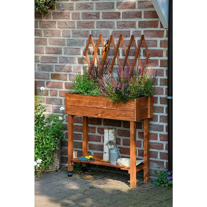 Dobar Hochbeet - L x B x H: 79 x 28,5 x 130 cm, Holz, Braun - Bild eines hochgezogenen Pflanzgefäßes aus Holz mit Pflanzen, das auf einem Untergestell mit Ablagefläche und Rädern steht.
