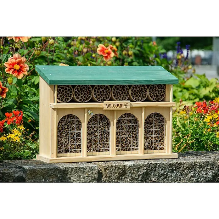 Dobar Insektenhotel Dublin - 44 x 13,5 x 30 cm, Holz, Braun/Grün - Dieses Bild zeigt ein Insektenhotel aus Holz mit einem grünen Dach, das auf einer Steinmauer vor einem Hintergrund aus Blumen steht.