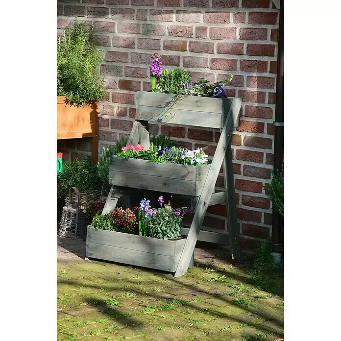 Dobar Pflanzkasten - L x B x H: 60 x 70 x 90 cm, Holz, Grau - Ein grauer, gestufter Holzpflanzkasten mit bunten Blumen und Pflanzen auf einer Terrasse vor einer Ziegelwand.