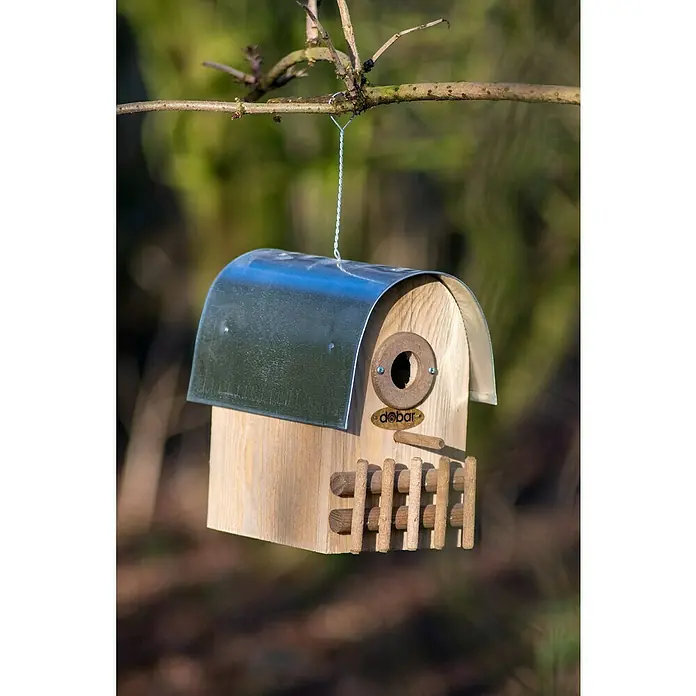 Dobar Nistkasten Rundhaus - 14 x 20 x 22 cm, Holz, Braun/Silber - Nahaufnahme eines hölzernen Vogelhauses mit Metallabdeckung, aufgehängt an einem Ast, das eine natürliche und schützende Umgebung für Vögel bietet.