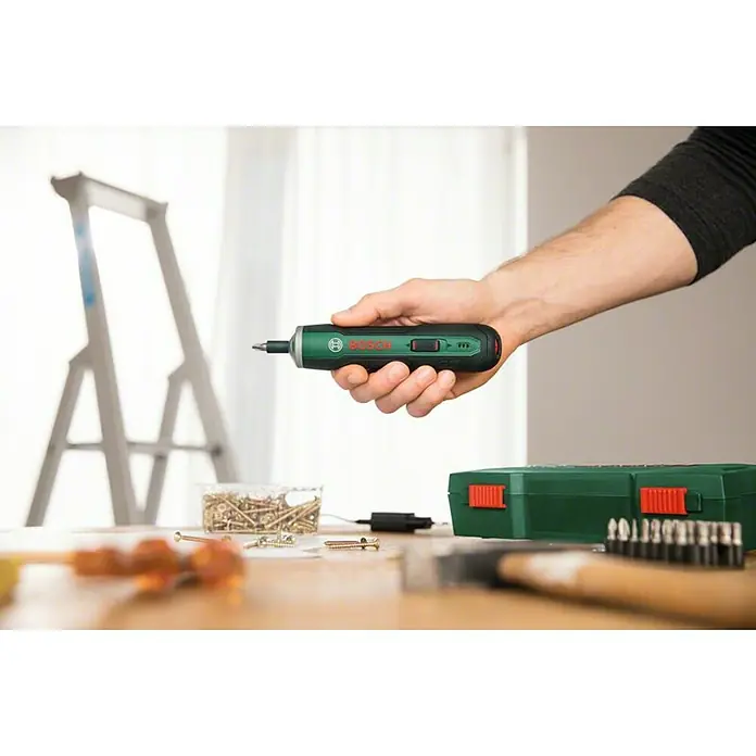 Bosch Akkuschrauber PushDrive - 3,6 V, 10 Schrauberbits - Akkuschrauber in der Hand vor Werkbank mit Werkzeug und Leiter.