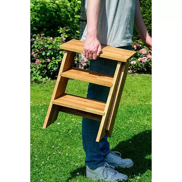 Dobar Klapptritt - L x B x H: 42 x 54 x 45 cm - Eine Person trägt einen hellbraunen Holz-Klapptritt im Freien.