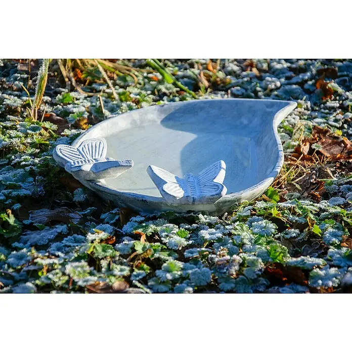 Dobar Vogeltränke Foglia - Weiß, Keramik - Nahaufnahme einer Vogeltränke in Tropfenform mit zwei Schmetterlingen, umgeben von frostbedeckten Blättern.