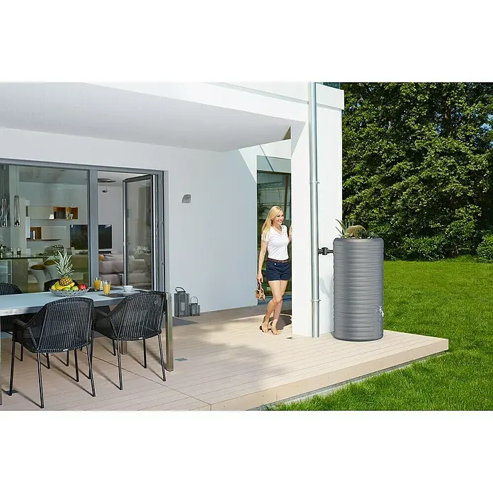 Garantia Classic Line Regenspeicher Nordic 2 in 1 - 300 l, Steingrau - Eine graue Regentonnen mit Pflanzschale steht neben einem modernen Haus. Sie dient als dekorativer Wasserspeicher für den Garten.
