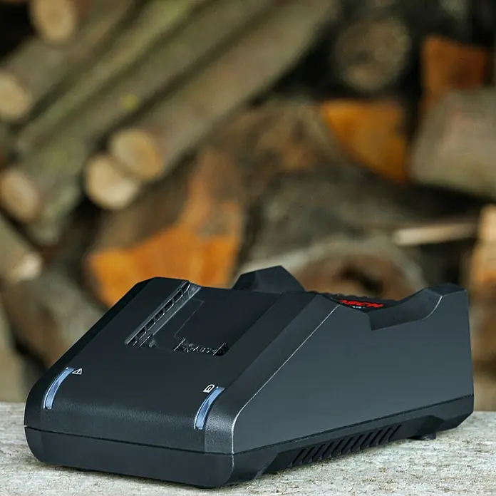 Bosch Power for All 36V Cargador de baterías - 36 V, Específico para: Baterías de 36 V 2 Ah / 4 Ah - La imagen muestra un cargador de batería negro con un fondo de leña apilada. El cargador tiene luces indicadoras LED azules.