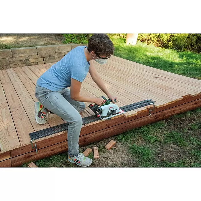Bosch Power for All 18V Akku-Handkreissäge UniversalCirc 18V-53 - 18 V, Ohne Akku, 4.300 U/min, Durchmesser Sägeblatt: 160 mm - Person schneidet Holzterrassenbretter mit weißer und grüner Bosch Handkreissäge und Führungsschiene, trägt Schutzbrille und Maske.
