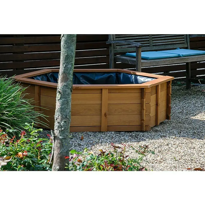 Dobar Hochteich Hexagon - L x B x H: 149 x 128,5 x 40 cm, Braun - Holz-Hochbeet mit schwarzer Folie ausgekleidet, umgeben von Gartenpflanzen und Kies. Eine Holzbank steht im Hintergrund.