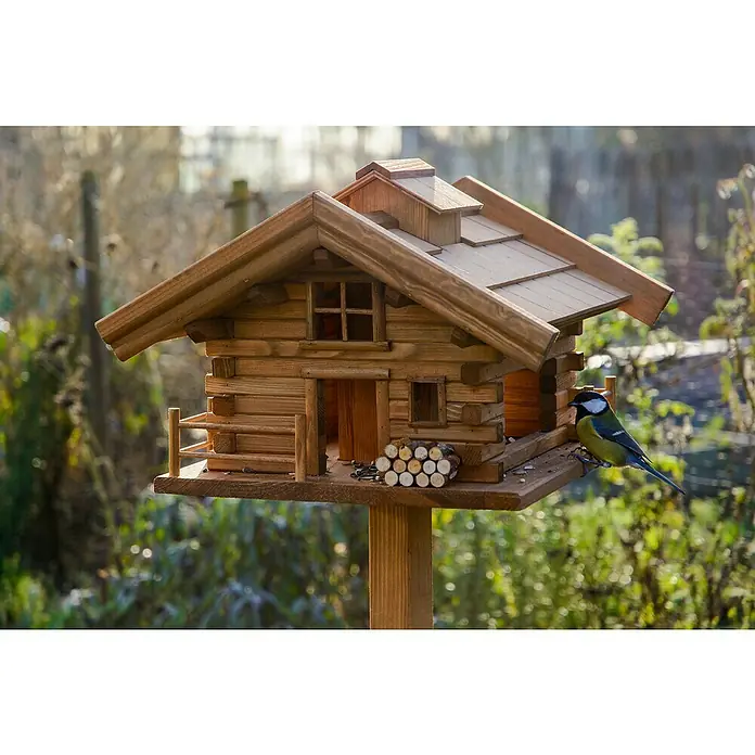 Dobar Vogelfutterhaus Tirol - L x B x H: 37 x 37 x 117 cm, Braun, Holz - Ein detailreiches Vogelhaus im Blockhausstil mit einem bunten Vogel, der darauf sitzt, umgeben von verschwommenem Grün.