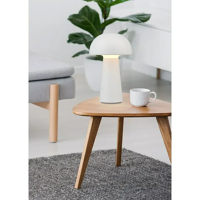 Trio Leuchten Akku-Tischleuchte Lennon - 2 W, Weiß, Warmweiß - Pilzförmige Tischleuchte in Weiß auf einem Holztisch mit einer Kaffeetasse, die eine gemütliche und moderne Atmosphäre schafft.