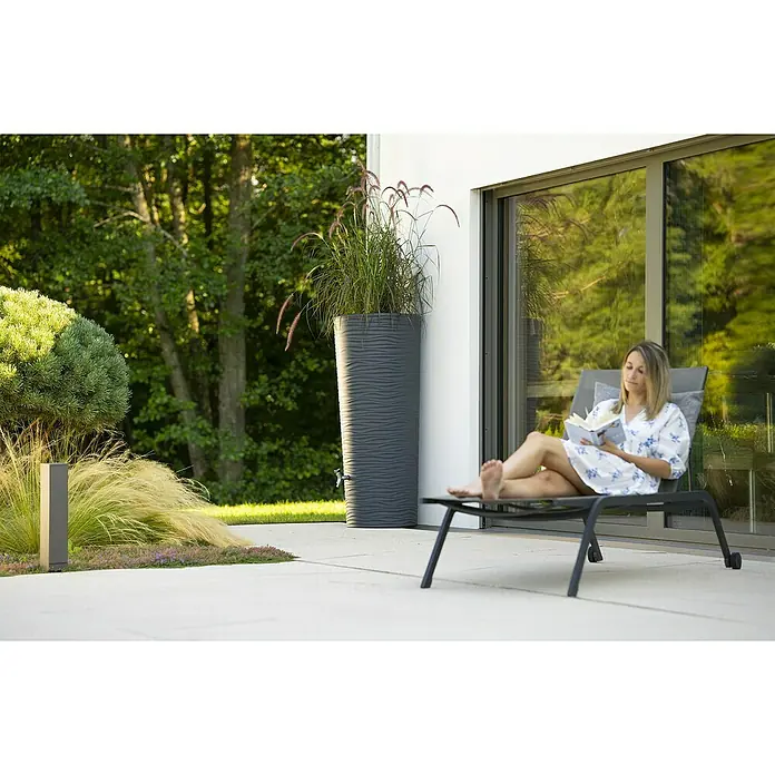 Garantia Modern Line Regenspeicher Natura 2 in 1 - 350 l, Graphite grey - Eine Frau entspannt auf einer Liege neben einem grauen Regenwassertank mit Bepflanzung. Ideal für Gartenbewässerung!