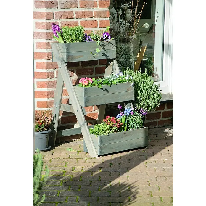 Dobar Pflanzkasten - L x B x H: 60 x 70 x 90 cm, Holz, Grau - Ein graues, dreistufiges Pflanzenregal mit bunten Blumen und Pflanzen steht auf einer Terrasse vor einer Backsteinmauer.