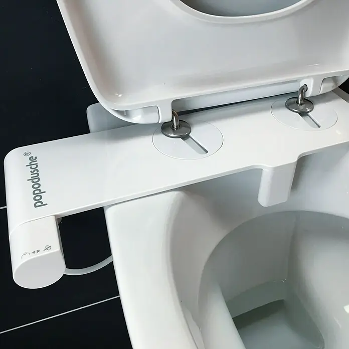 Popodusche WC-Aufsatz - Weiß - Nahaufnahme einer weißen Popodusche-Bidet-Befestigung, die an einer Toilette installiert ist und für persönliche Hygiene sorgt.