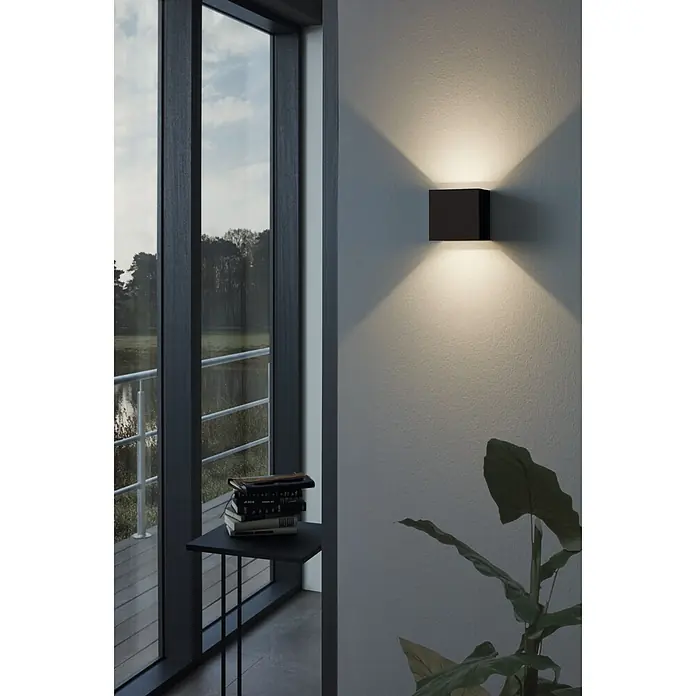 Eglo Aplique exterior LED Calpino - 6,6 W, 10,5 x 10,5 x 10,5 cm, Antracita, IP54 - Una lámpara de pared cúbica negra moderna irradia luz cálida hacia arriba y hacia abajo, acentuando una pared brillante en la habitación.