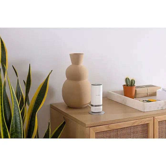 Bosch Smart Home Innenkamera Eyes II - Netzbetrieben, L x B x H: 160 x 72 x 160 mm, 1.920 x 1.080 Pixel (Full HD), Reichweite Funk: 0 m - 99 m - Nahaufnahme eines Bosch-Luftreinigers auf einem Sideboard mit Pflanzen und Dekor, der saubere Luft und stilvolles Design vereint.