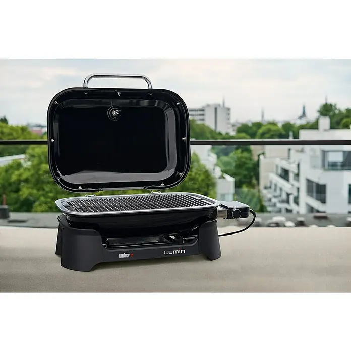 Weber Barbacoa eléctrica Lumin 2000 - Superficie de la parrilla (An x Pr): 49 x 33 cm, 2,2 kW, Negro - Primer plano de una parrilla eléctrica Weber Lumin con la tapa abierta en un balcón, destacando las rejillas y los controles.