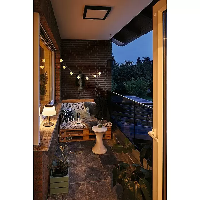 Paulmann Solar-Dekoleuchte Lillesol - 0,8 W, Edelstahl, IP44 - Eine kleine weiße tragbare Laternenlampe spendet stimmungsvolles Licht auf einem gemütlichen Balkonsofa.