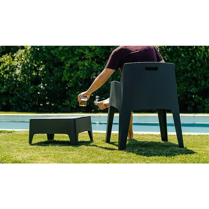 Set de muebles de jardín Master -  - Una silla de jardín y una mesa auxiliar minimalistas de plástico oscuro están colocadas sobre césped junto a una piscina, con una persona sosteniendo una bebida.