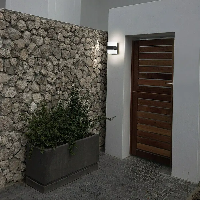 Forlight Aplique exterior LED Opalo - 14,3 W, L x An x Al: 11 x 8 x 12 cm, Antracita, Blanco neutro - Primer plano de una lámpara de pared exterior moderna junto a una puerta de madera, que emite un brillo cálido.